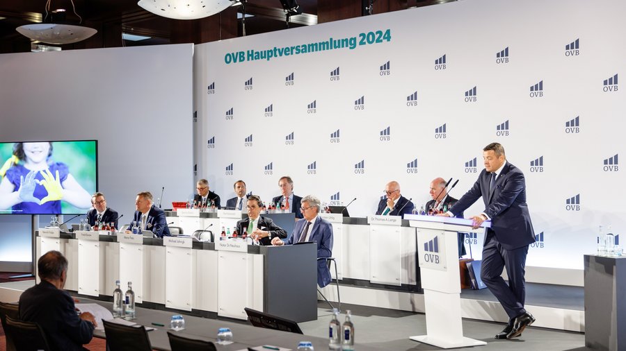 Podium mit mehreren Vorstandsmitgliedern bei der OVB Hauptversammlung 2024, der CEO Mario Freis steht am Rednerpult.