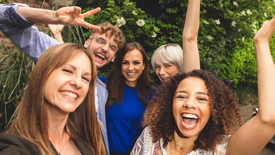 Fünf Freunde stehen eng beieinander und lachen in die Kamera