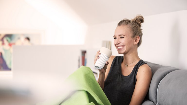 Junge Frau mit Decke und Tee auf der Couch.