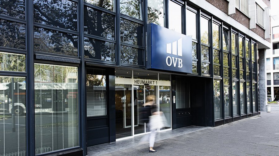 Außenansicht eines modernen Bürogebäudes mit OVB-Logo über dem Eingang, eine Person mit Tasche läuft am Gebäude vorbei.
