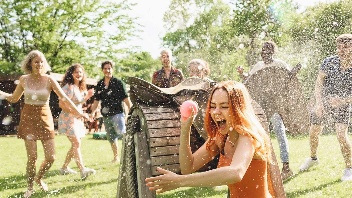Eine Gruppe junger Leute macht eine Wasserschlacht, während sich eine Frau versteckt