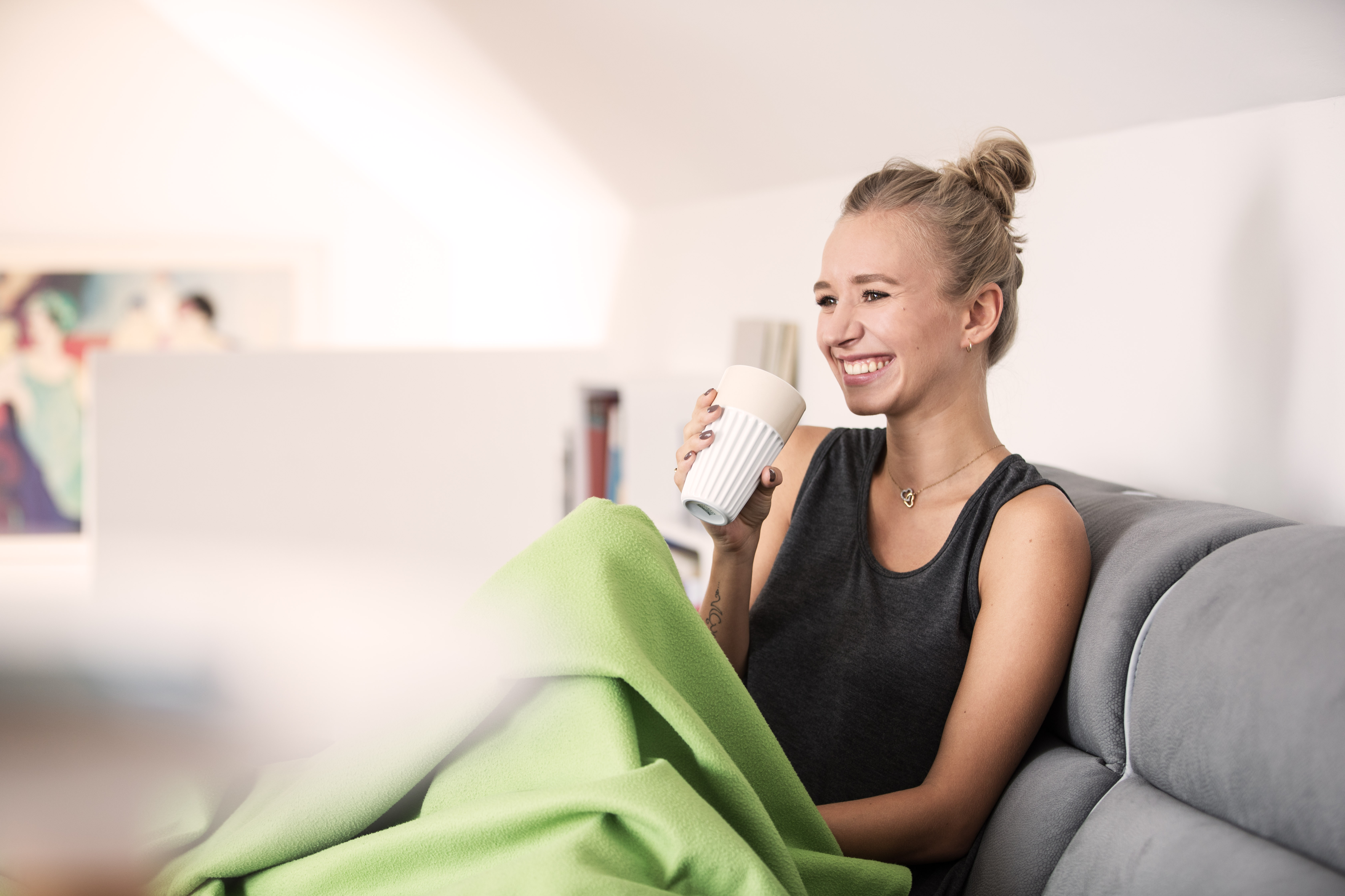 Zusatzkrankenversicherung: Frau sitz mit Decke und Becher auf einem Sofa