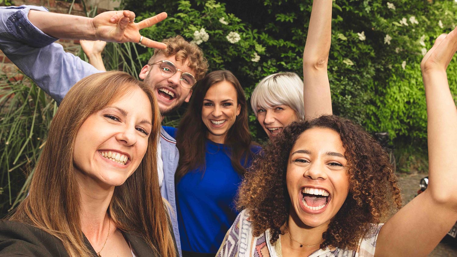 Urlaub mit Freunden planen – so geht’s Fünf Freunde stehen eng beieinander und lachen in die Kamera