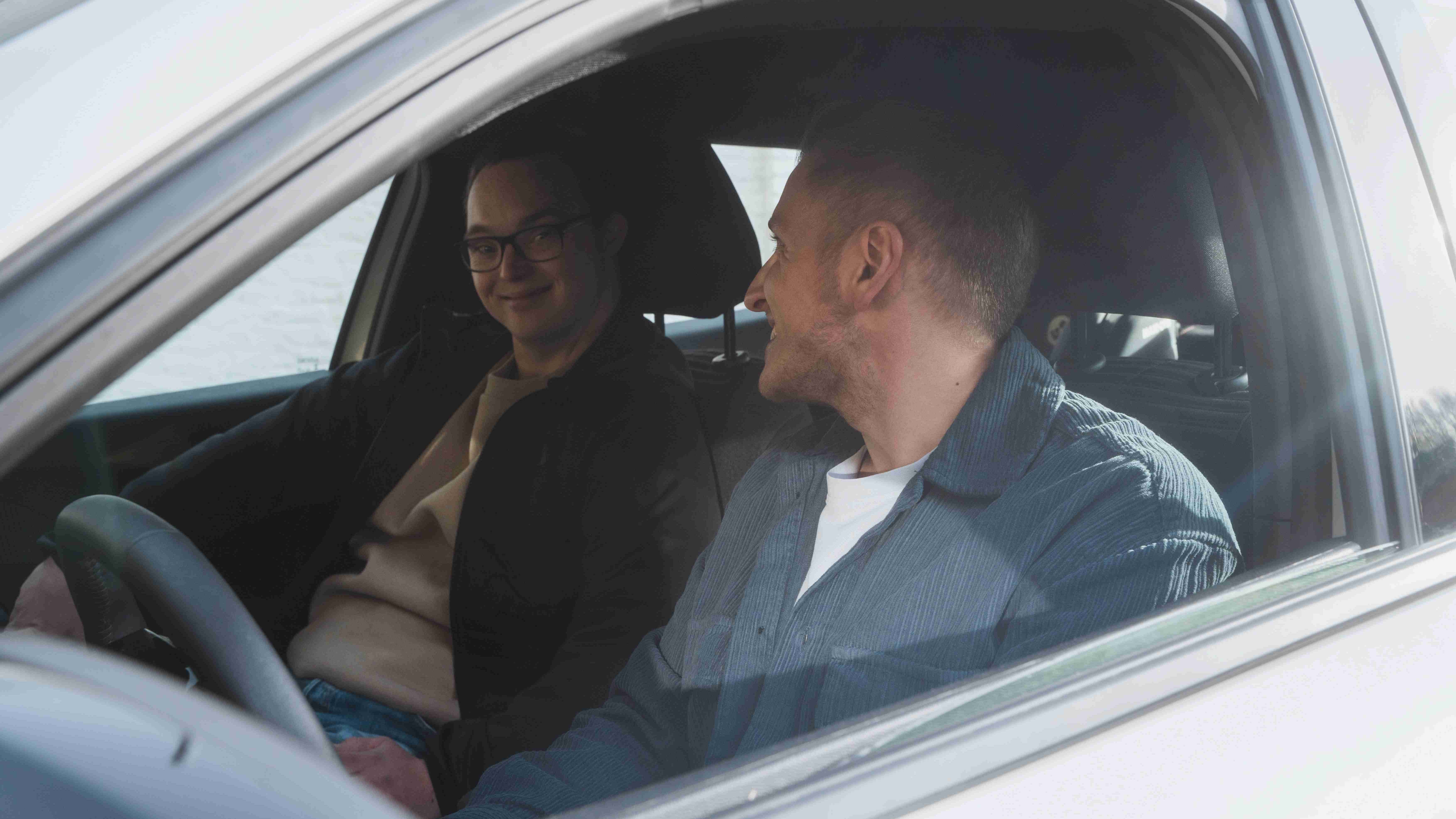 Zwei junge Männer sitzen in einem Auto und lächeln sich an