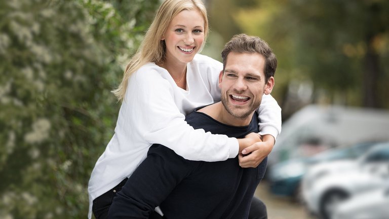 Junge Frau lachend auf dem Rücken ihres Partners.
