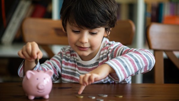 Kind mit Sparschwein und Geldmünzen – monatliche Fixkosten im Haushalt Kind mit Sparschwein und Geldmünzen – monatliche Fixkosten im Haushalt