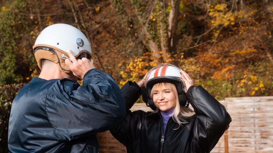 Zwei junge Menschen stehen im Freien und ziehen einen Motorradhelm an.
