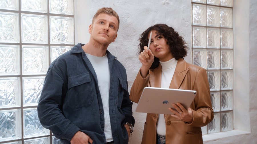 Mann blickt hoch, Frau mit Tablet erklärt dem Mann etwas.