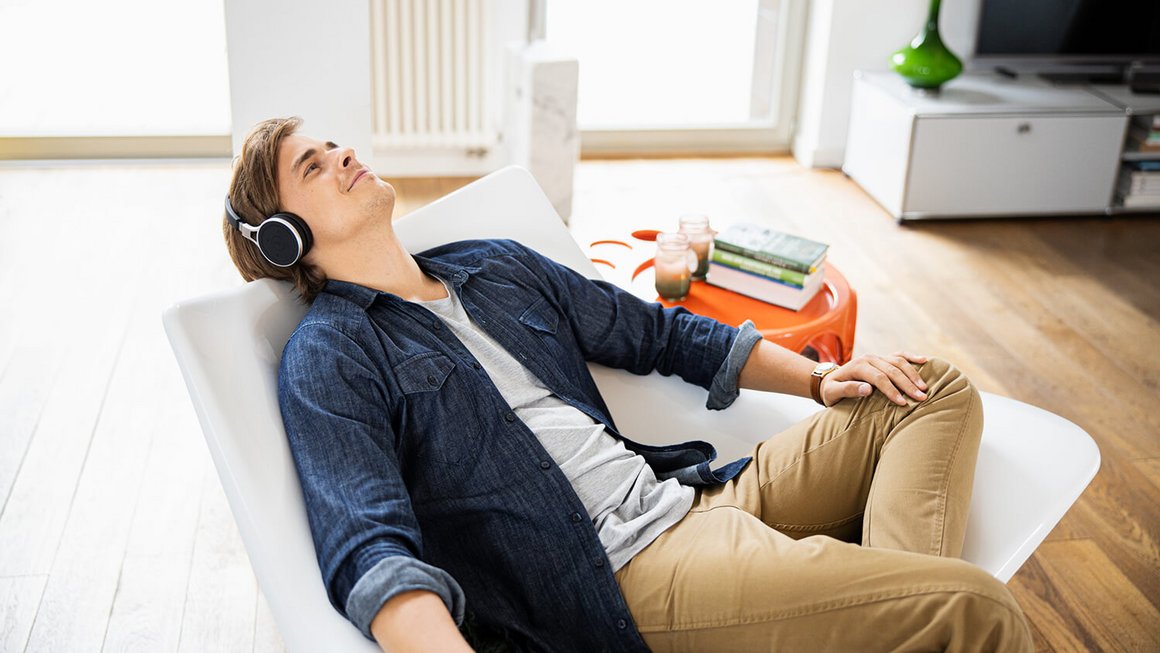 Junger Mann lehnt sich zurück und hört Musik in der ersten eigenen Wohnung Junger Mann lehnt sich zurück und hört Musik in der ersten eigenen Wohnung