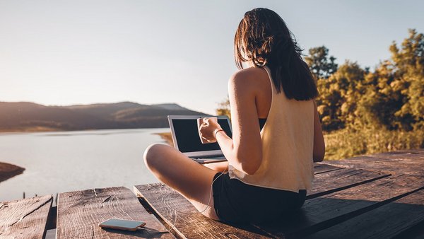 Mobiles Arbeiten im Ausland – Frau sitzt mit Laptop am See Mobiles Arbeiten im Ausland – Frau sitzt mit Laptop am See